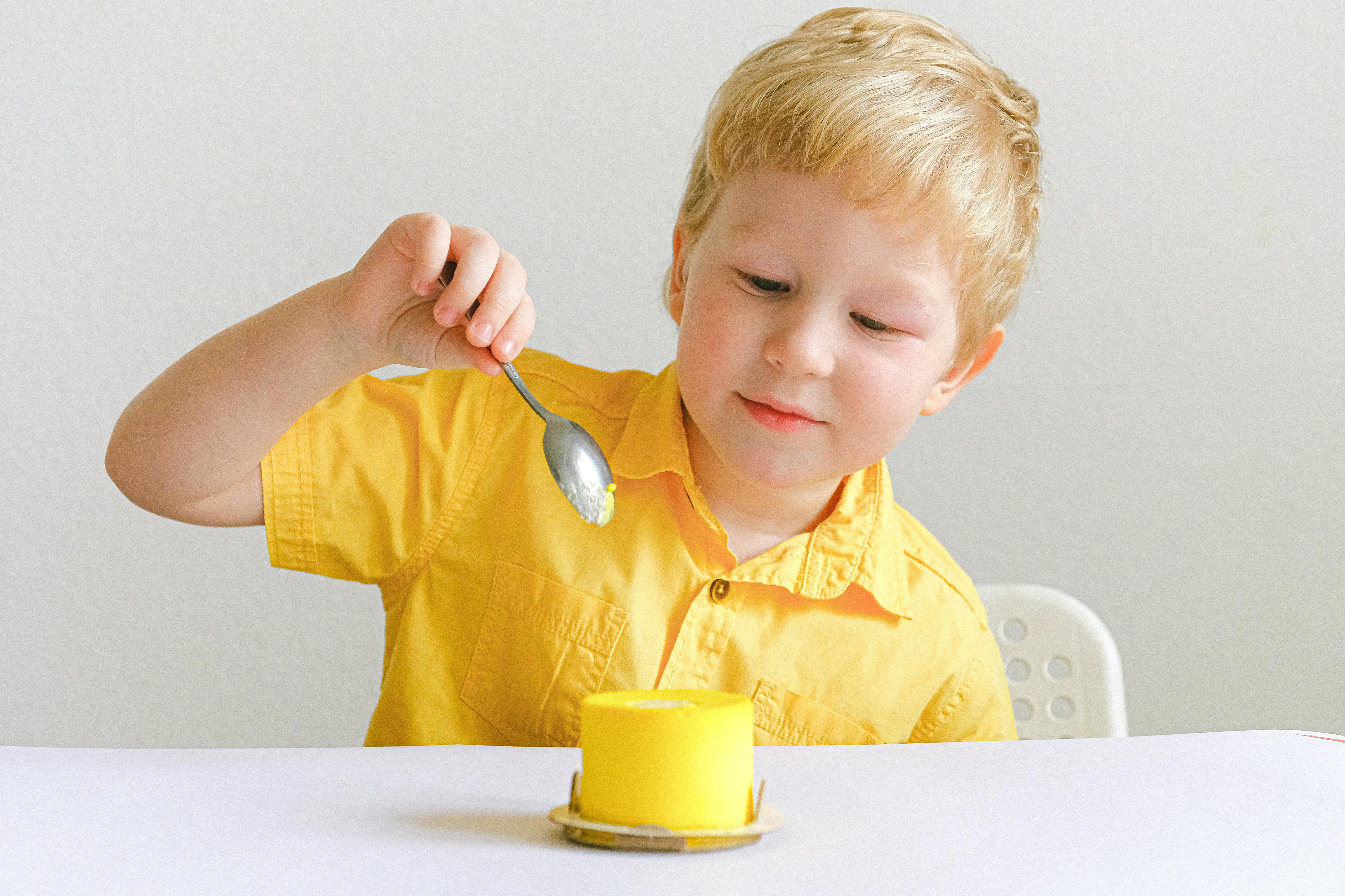 可爱的孩子在明亮的环境里用勺子吃着黄色甜点