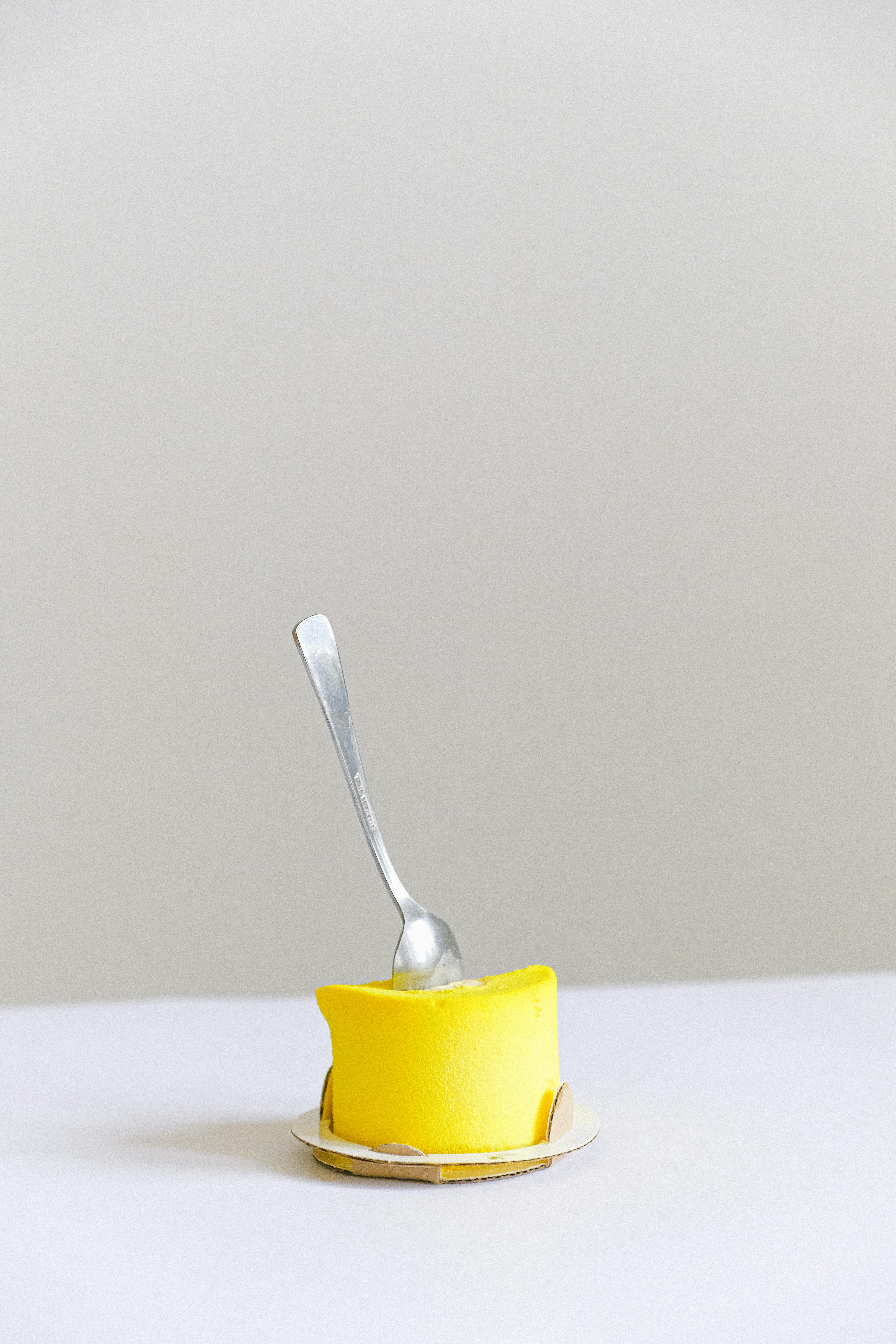 在简单的白色背景上，一把勺子置于明亮的黄色甜点之上，体现了极简主义的设计