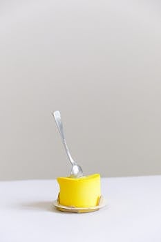 在简单的白色背景上，一把勺子置于明亮的黄色甜点之上，体现了极简主义的设计