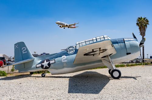 Free A vintage fighter aircraft on display with a modern commercial jet flying above, set against a clear blue sky. Stock Photo