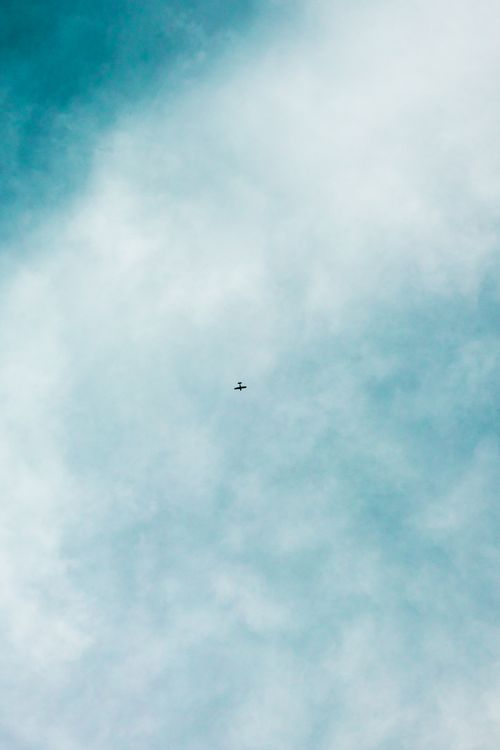 Free An isolated airplane flying through a vast blue cloud-filled sky, conveying freedom. Stock Photo