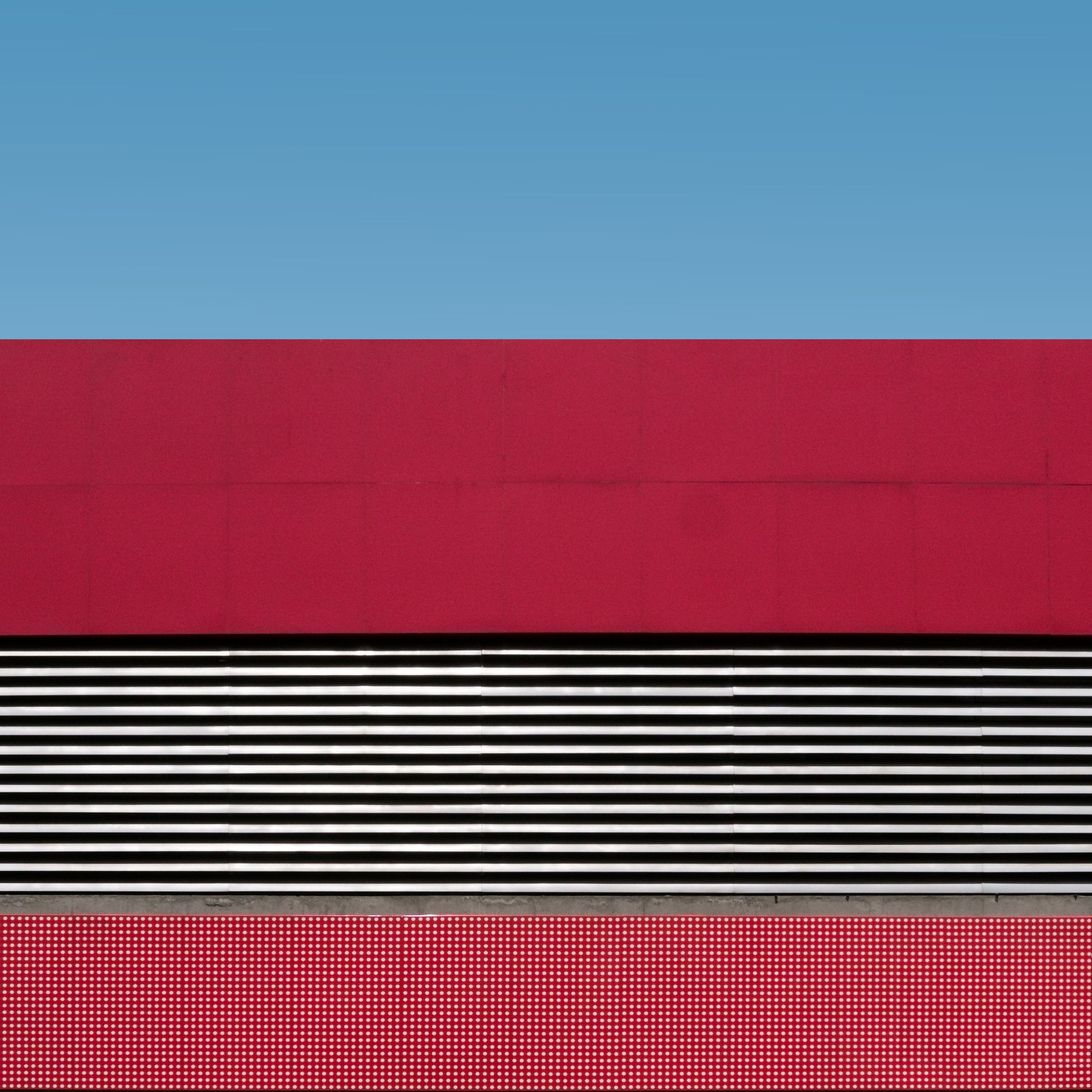 A minimalist architectural photo featuring red and white patterns against a clear blue sky.