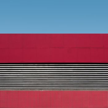 A minimalist architectural photo featuring red and white patterns against a clear blue sky.