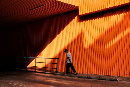 A man walks by a vibrant orange corrugated wall in Bandung creating dramatic shadows.