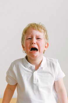 一个幼儿穿着白衬衫，在室内哭泣，情绪很激动