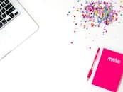 明亮的公寓里放着一台笔记本电脑、一本标有“惊人”的粉色笔记本、一支钢笔和一些彩色五彩纸屑