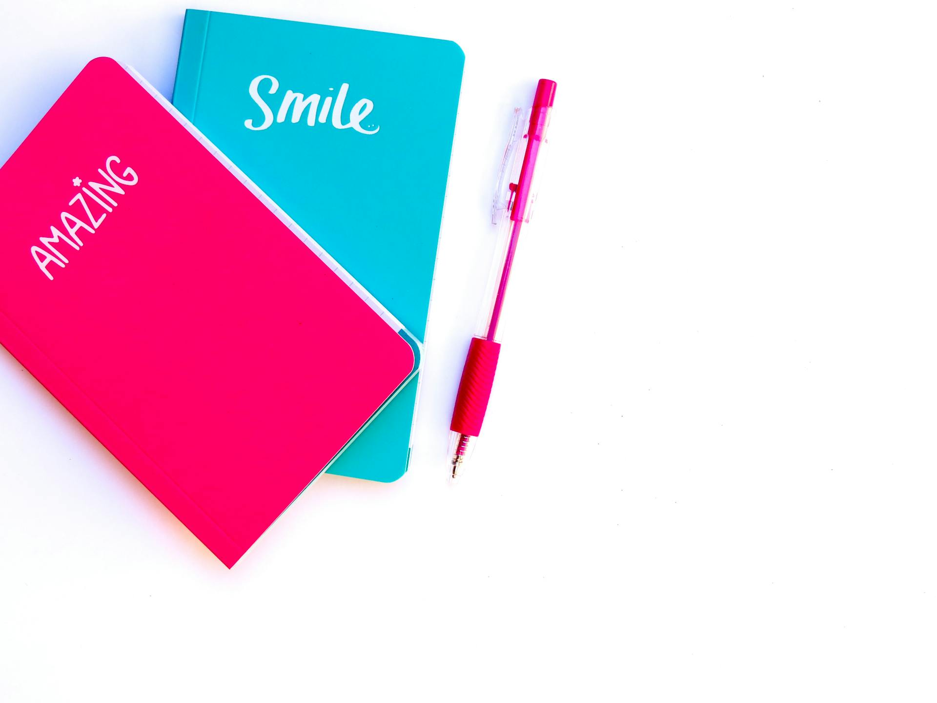 Colorful flat lay with turquoise and pink notebooks and matching pen on white background.