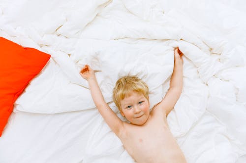 Topless Boy Lying On White Bed