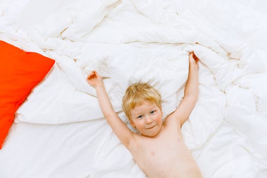 Adorable child relaxing joyfully on white bedding with a bright red pillow, creating a warm and cheerful atmosphere.