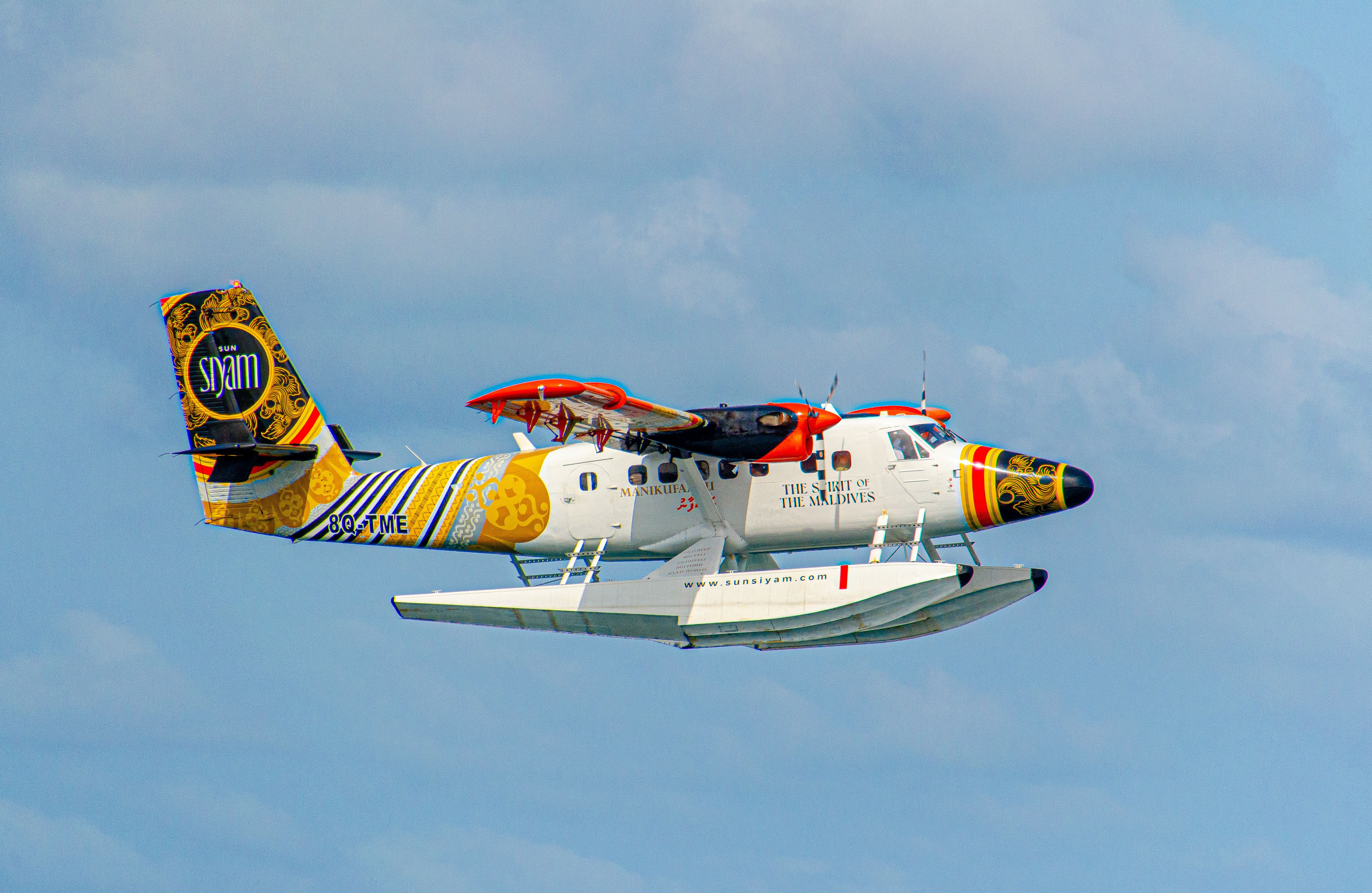 Vibrantly painted seaplane flying over the clear skies of Maldives, showcasing its colorful design.