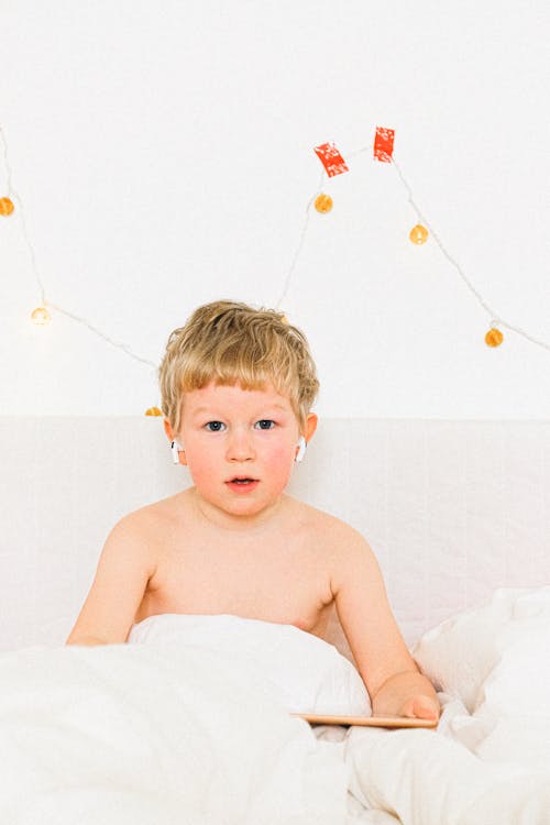 Topless Boy Sitting On White Bed