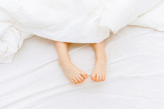 孩子可爱的脚从白色毯子里伸出来，传递着温暖与舒适