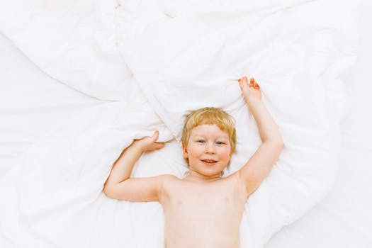 Joyful child lying on soft white bed sheets, smiling and relaxed.