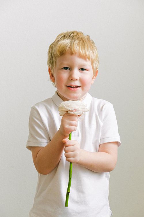 Free Blond child smiling while holding a white flower against a soft background. Stock Photo