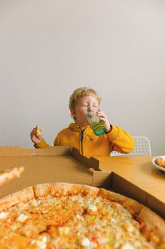 一个穿着黄色夹克的男孩正在家里享用披萨和饮料，营造出舒适的用餐氛围