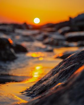 A vibrant sunset reflecting over rocky shoreline, capturing the golden hues of the sky.