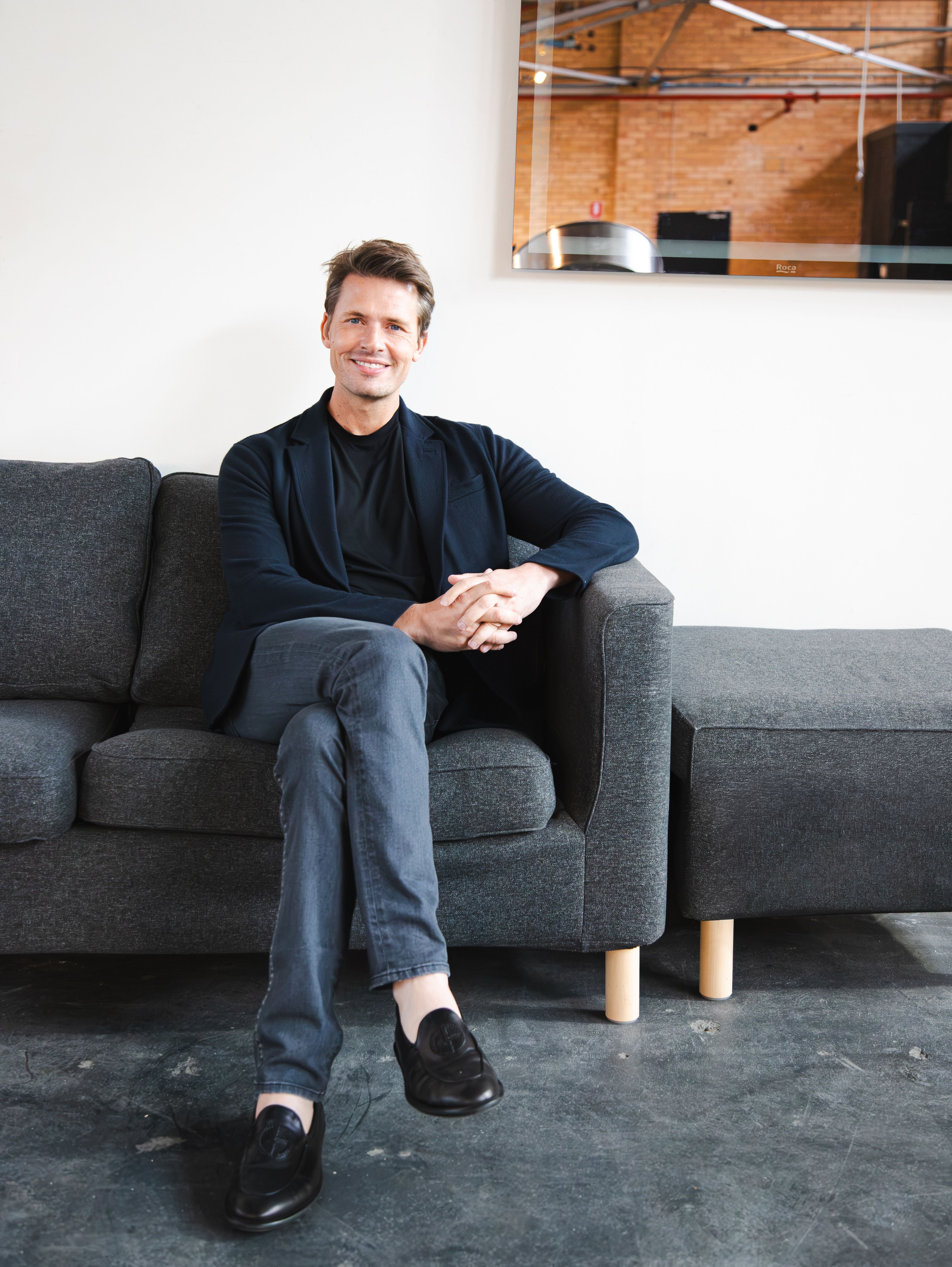 Portrait of a smiling man seated on a couch in a modern office setting, highlighting professional ambiance.