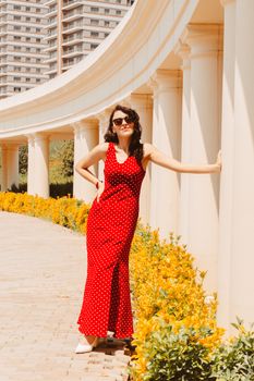 Stylish woman in a red polka dot dress poses by a curved colonnade in Baku, Azerbaijan.