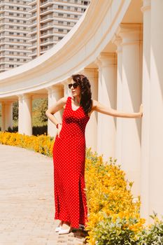 Stylish woman in a red dress with polka dots poses by elegant architecture in Baku.