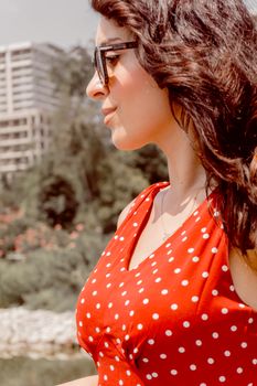 Profile of a woman in a red polka dot dress enjoying a sunny day outdoors in Baku.
