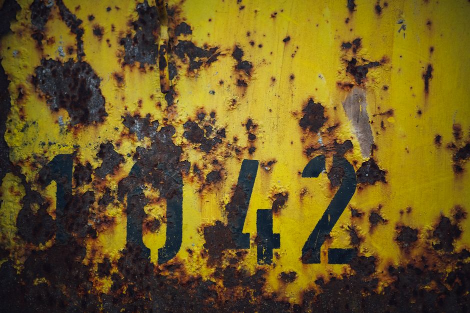 Close-up of a corroded yellow metal surface with rust and the number 1042.