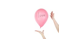 粉色气球在双手之间漂浮，上面写着“爱”字，象征着感情