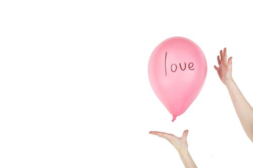 Free Pink balloon with the word 'love' floating between hands, symbolizing affection. Stock Photo