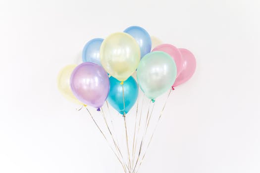 A cluster of colorful pastel balloons floating with a minimalistic white backdrop.
