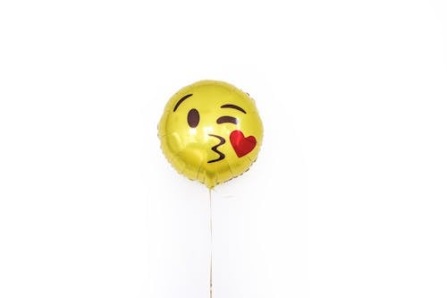 Free Golden glossy round shaped balloon with smiley kissing heart face filled with helium arranged on white background isolated in studio Stock Photo