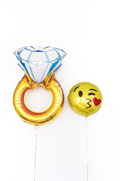 Pair of foil glossy balloons in shape of diamond ring together with smiling face kissing heart isolated on white background