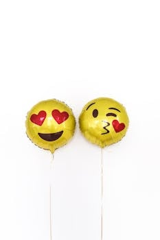 Two yellow emoji balloons with playful expressions on a white background.