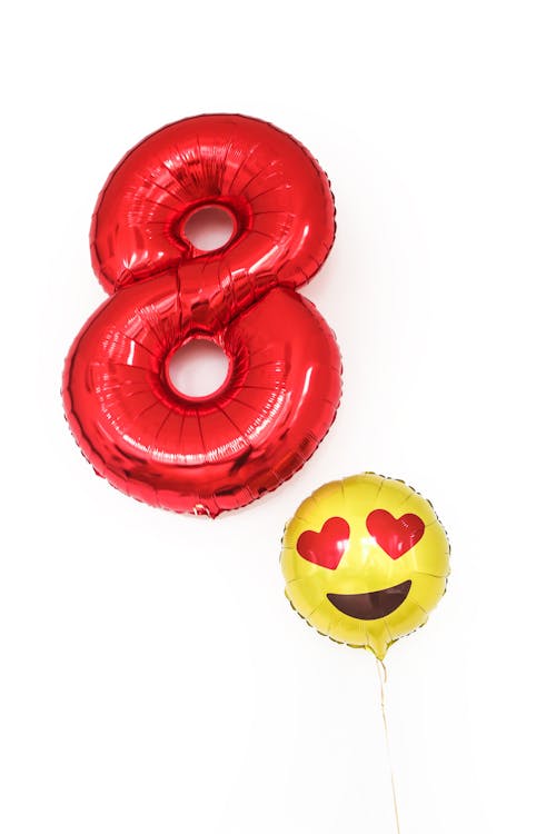 Big red balloon in shape of number eight with small ballon with emoticon with hearts placed on white background