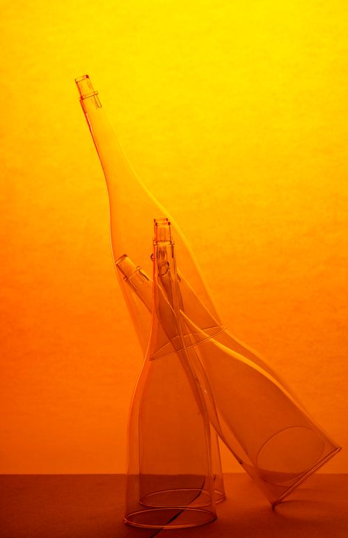 Free Elegant arrangement of translucent glass bottles against a vibrant orange background, showcasing creative still life photography. Stock Photo