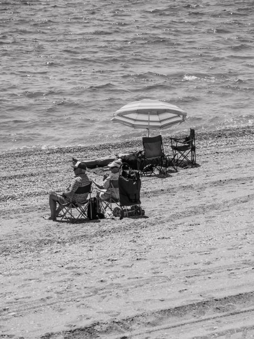 Free Relaxing on a pebble beach with chairs and an umbrella by the ocean. Stock Photo