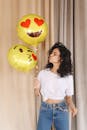一位穿着白色休闲衬衫和蓝色牛仔裤的年轻女士，在明亮的房间里撅起嘴唇，看着亮黄色的气球