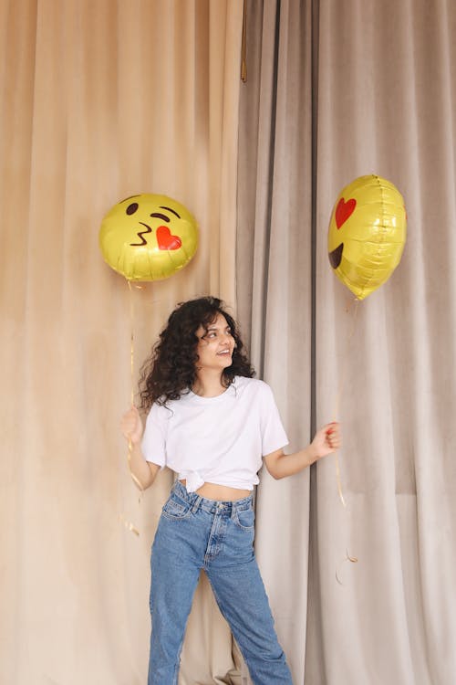 Smiling young lady holding balloons while standing near curtains in modern studio