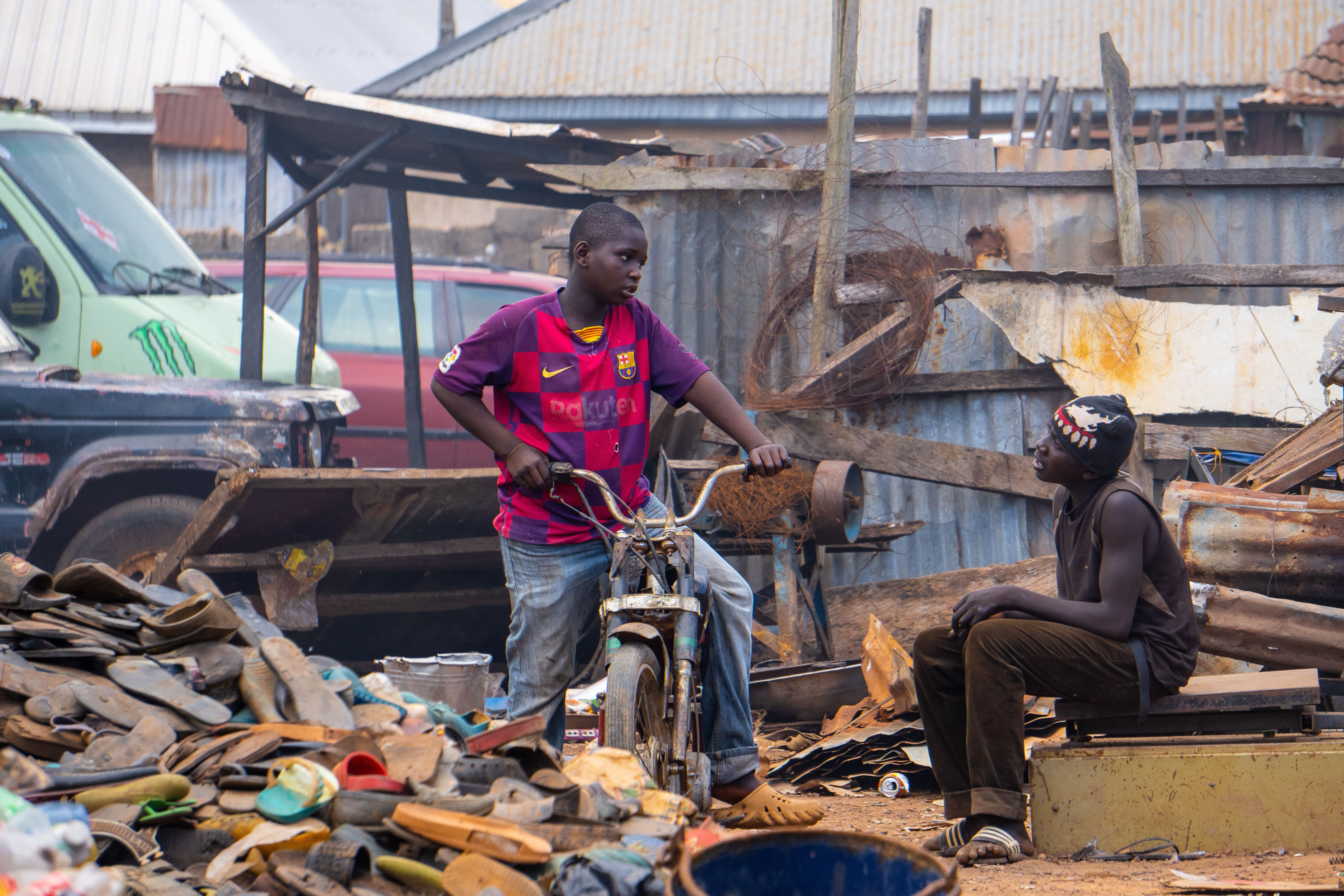 Two individuals interact at a bustling scrap yard, highlighting urban life's essence.