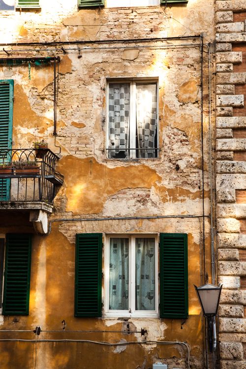 Free A close-up of a weathered European building facade with green shutters and textured brickwork. Stock Photo
