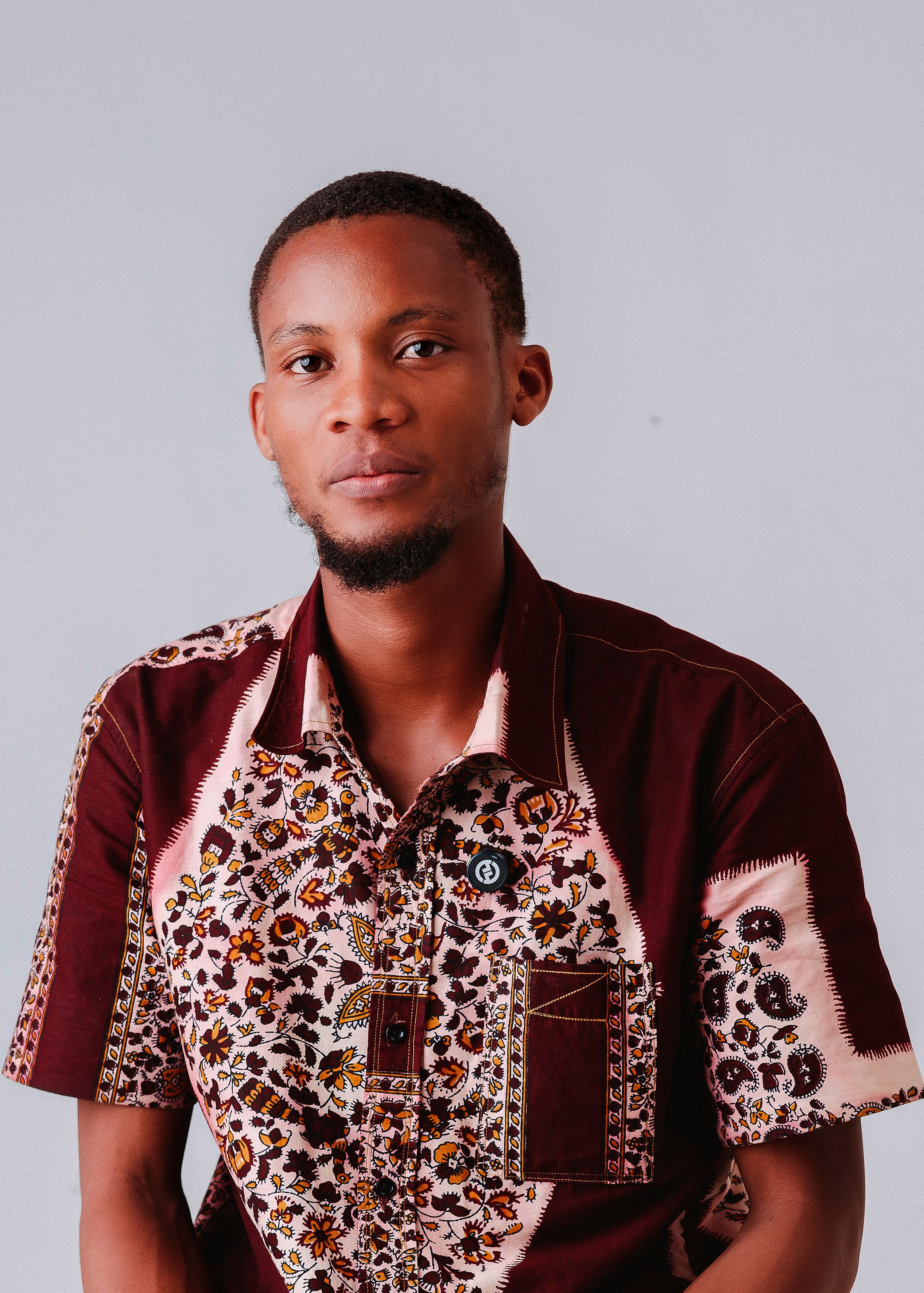 Young man in colorful traditional African shirt on a neutral background.