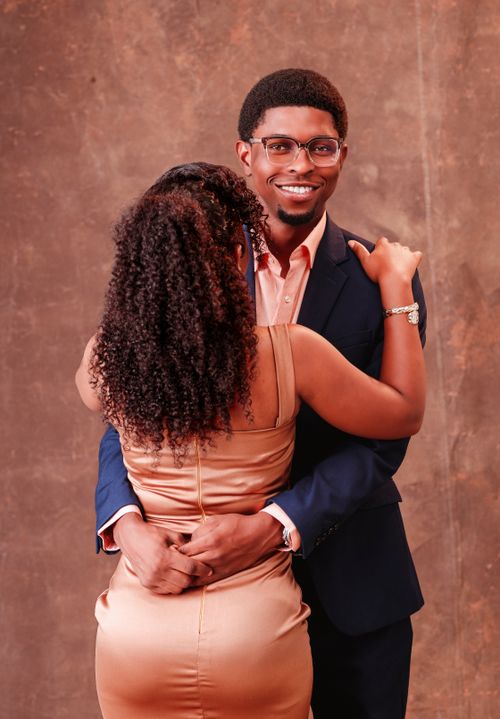 Free Stylish couple sharing a warm embrace in elegant attire against a textured backdrop. Stock Photo