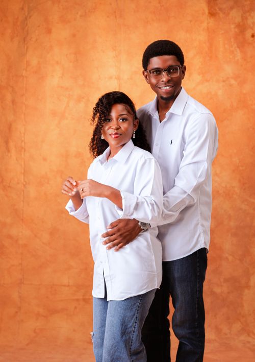 Free A cheerful couple in white shirts posing with a warm orange backdrop. Stock Photo