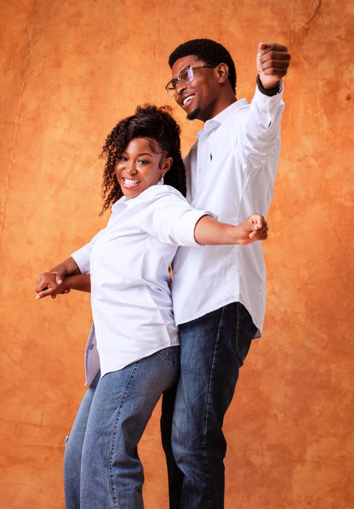 Free A happy couple wearing casual clothes dances against a warm-toned background, exuding joy and energy. Stock Photo