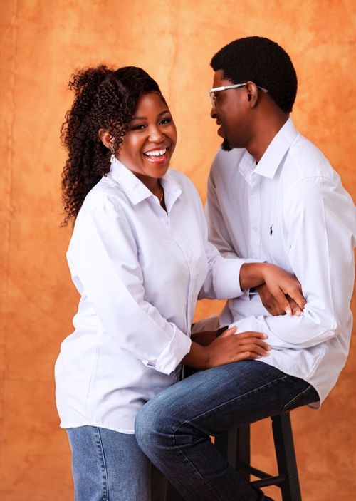 Free Joyful couple in white shirts against a warm orange backdrop, sharing a laugh. Stock Photo