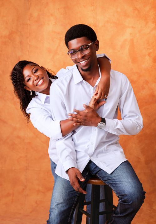 Free Smiling couple embracing and posing together in studio with orange backdrop. Stock Photo