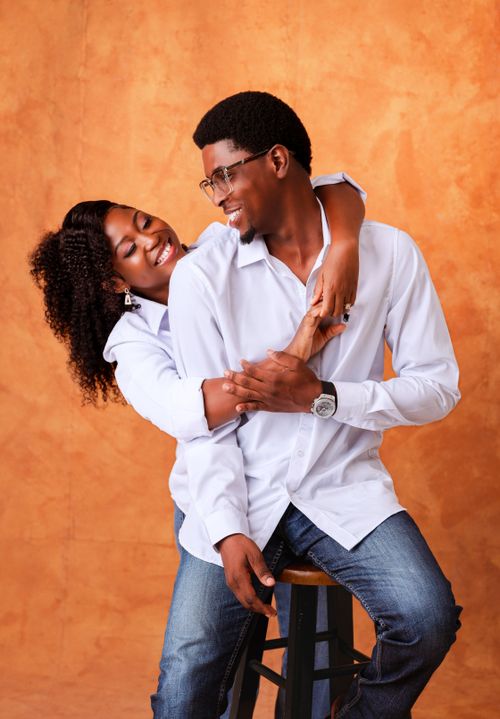 Free Cheerful African couple embracing and smiling against a warm orange backdrop. Stock Photo