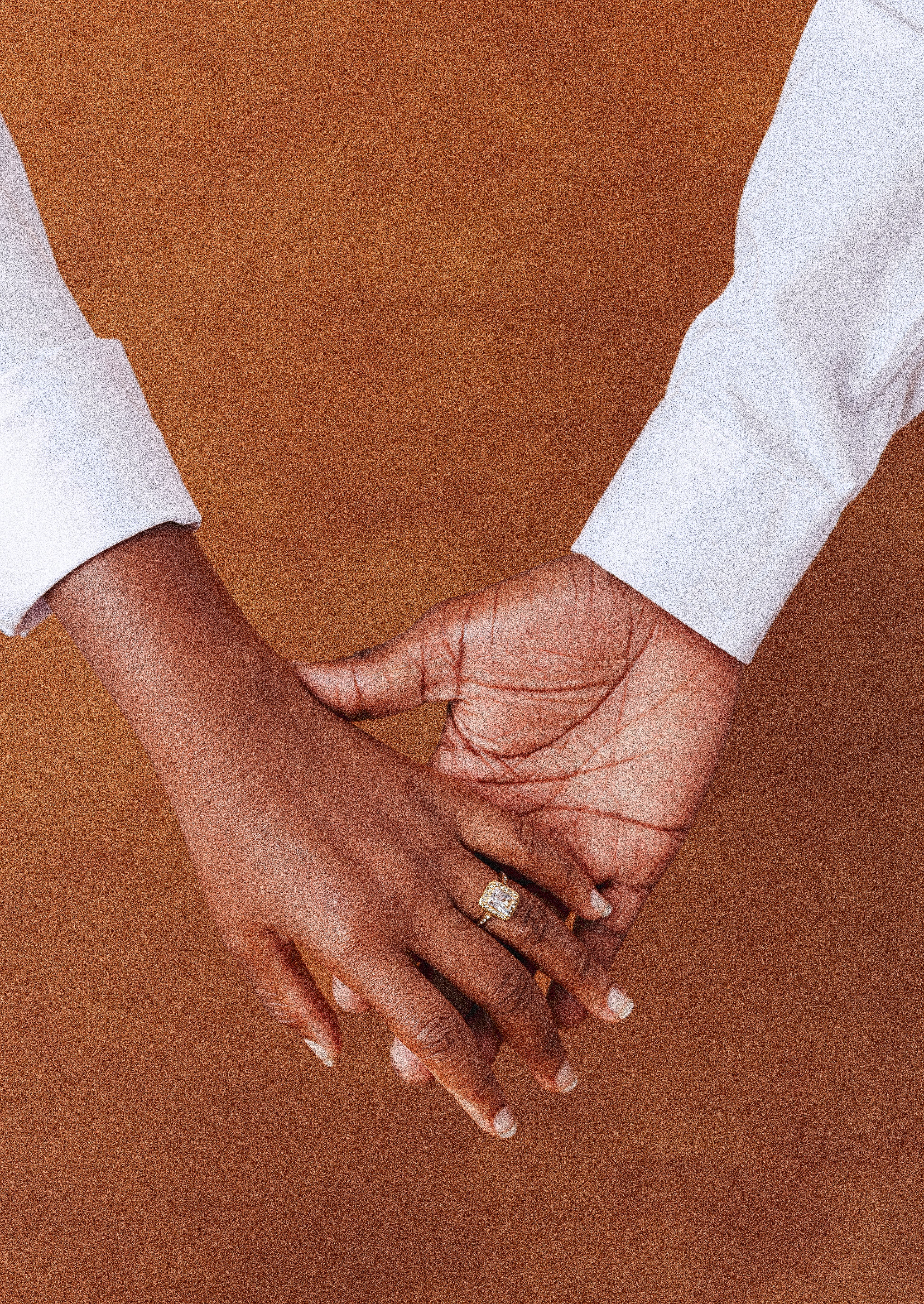 A couple's hands tenderly clasped with an elegant engagement ring visible.