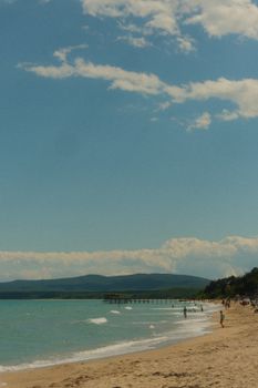 Serene beach with turquoise water, mountains, and a distant pier under a clear sky.