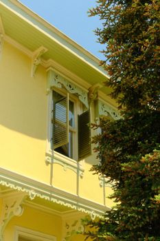 Charming Victorian house corner with an open window surrounded by greenery.