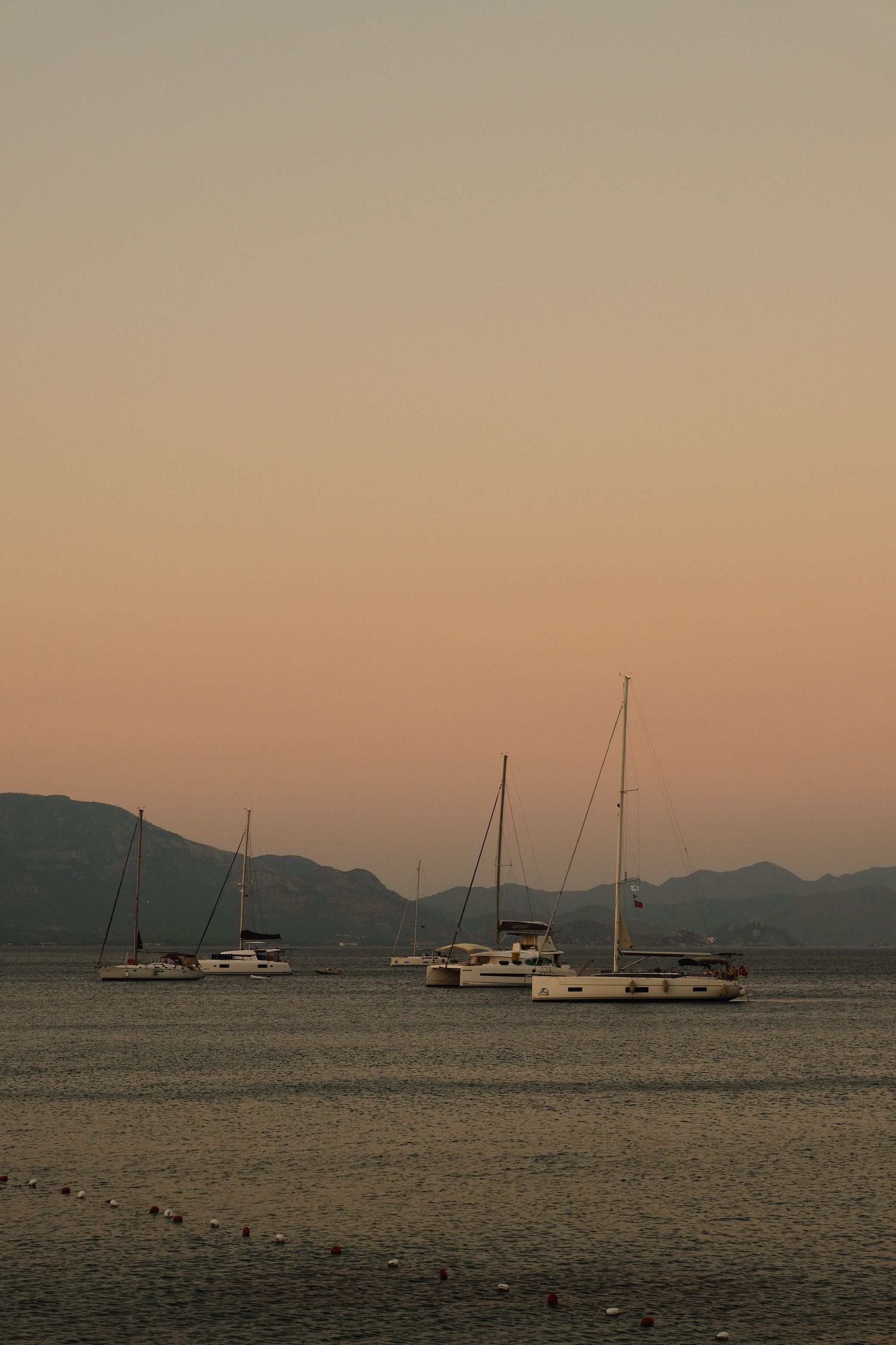 Tranquil scene of sailboats at sunset with a pastel sky over calm waters.