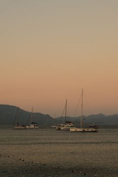 Tranquil scene of sailboats at sunset with a pastel sky over calm waters.